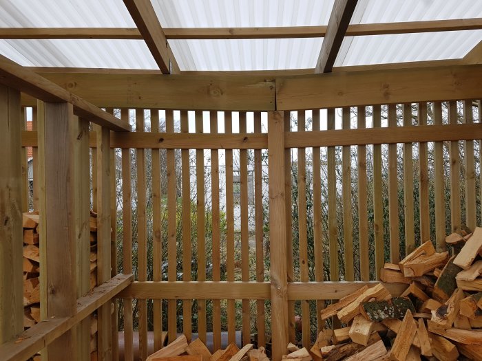 Vedbodens inre med träreglar och staplad ved, visar en skarv på stolpen och bärlinan som nästan nuddar markduken.