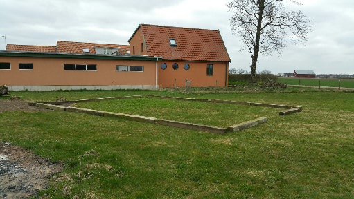 Planerad lekplats markerad med byggtimmer på en gräsyta framför ett hus.