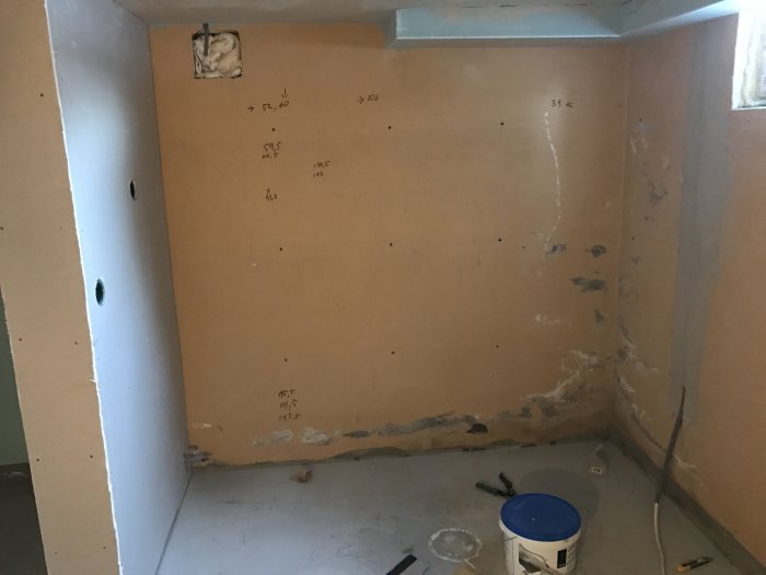 Badrum under renovering med oisolerade gipsskivor och synliga rörutskärningar.