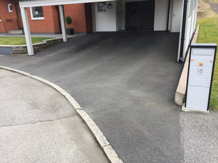 Nyrenoverad asfalterad uppfart till hus med carport och brevlåda, efter 'make-over' behandling.