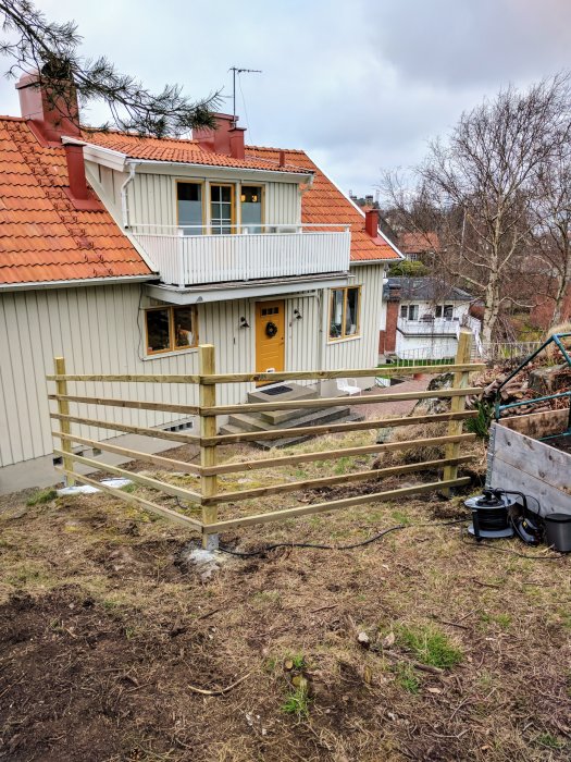 Nybyggt trästaket vid en sluttning nära ett gult hus för barnsäkerhet.