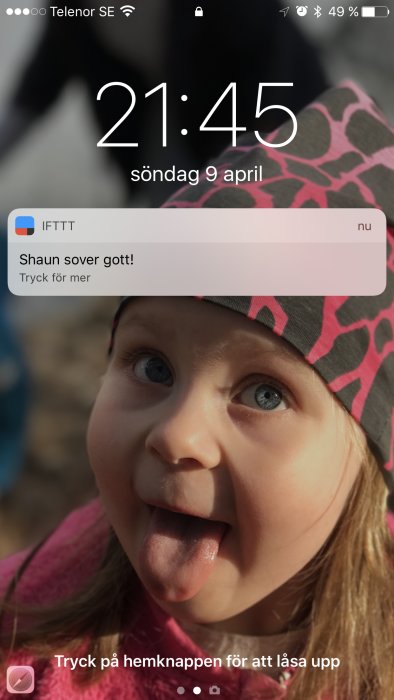 Skärmdump av en mobiltelefon som visar en notis med texten "Shaun sover gott!" över en bild av ett leende barn som räcker ut tungan.