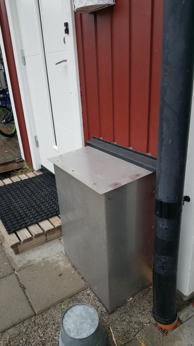 Bild på en fast installerad stolpsko på en betongplint bredvid en röd trävägg och ett stuprör.