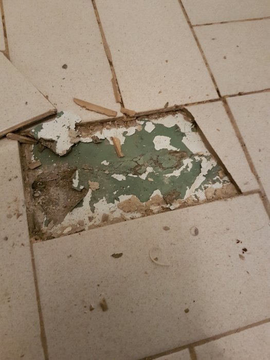 Skadat kakelgolv med bortbrutna plattor och exponerad underliggande yta.