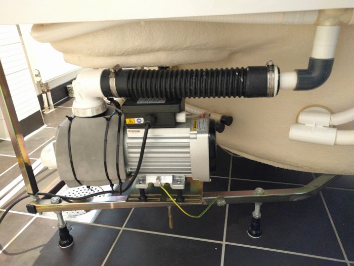 Nyinstallerad kylarslang och gummibussningar vid en badrumspump under badkar med ljudisolering.