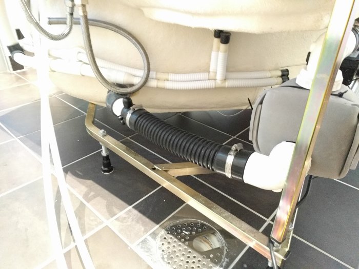 Undersidan av ett badkar med nyinstallerad kylarslang, gummibussningar och delar av pumphuset.