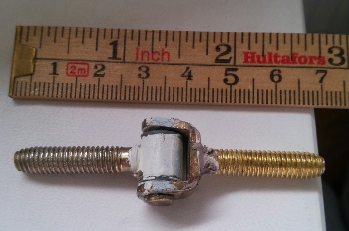Gängad bult med mutter och bricka bredvid en tumstock som mäter dess längd.