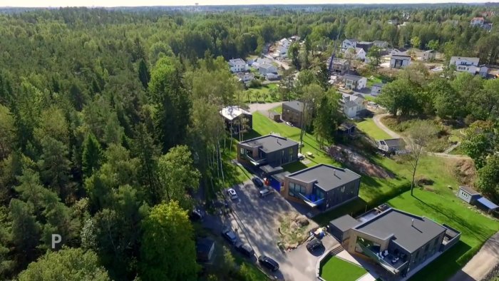 Flygbild över ett bostadsområde med tre moderna, likadana hus intill varandra, omgivna av grönska.