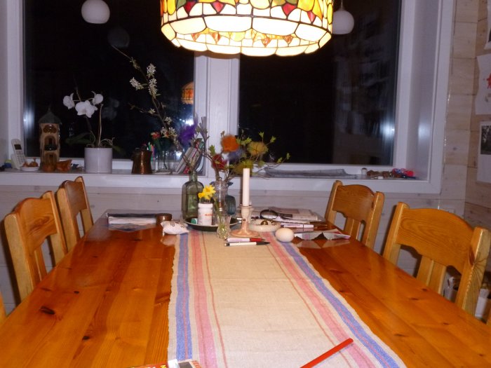 Vintage matbord från 1970-talet med trästolar och en färgglad lampa, nära ett fönster i ett hemtrevligt kök.