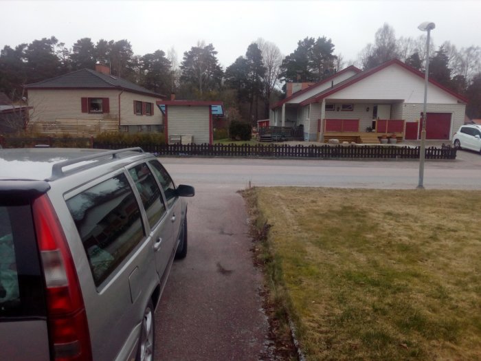 En gatuvy med två hus och en bilparkering, tänkt att visa takutstick före ombyggnad.