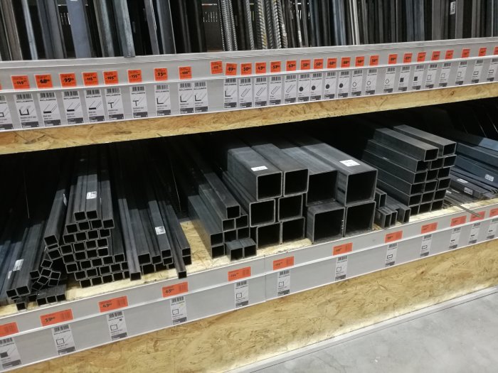 Stålprofiler i olika storlekar på hyllor i en bygghandel med prisetiketter.