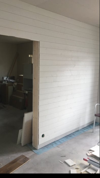 Nyinstallerad vit takpanel och vita väggpaneler i en under konstruktion varande inomhusmiljö med synlig eldragning och byggmaterial på golvet.