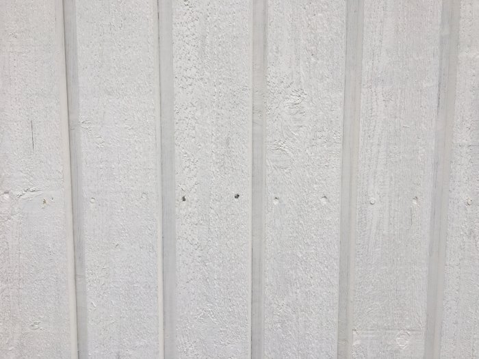 Vitmålad träpanelvägg med vertikala plankor och synliga spikar.