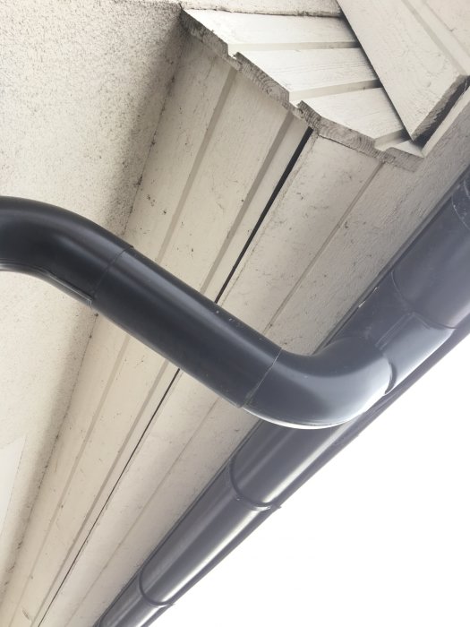 Närbild på takfot och stuprör mot en husvägg, som indikerar behov av målning eller underhåll.