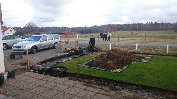 Person som förbereder mark med makadam för upphöjd rabatt vid parkering med bakgrund av landsbygd.