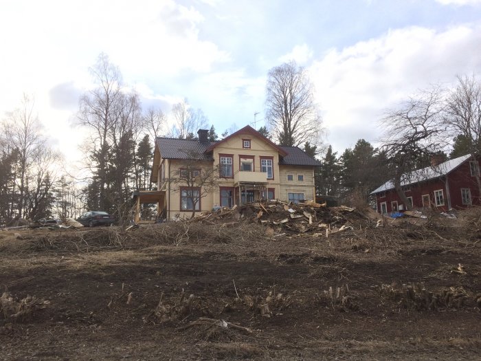 Hus med renoverat veranda och rensad trädgård med högar av grenar och avfall.