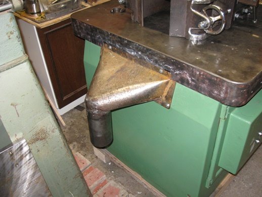 Nyinstallerad spåntratt i metall utgår från arbetsbänk och leder neråt mot golvet i en verkstadslokal.