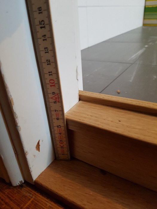 Tumstock visar en 70 mm nivåskillnad vid dörrtröskeln till ett badrum, olämplig för rullstolsåtkomst.