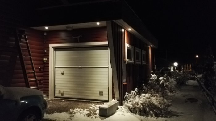 Nyrenoverad garagefasad på hus med rullport på kvällen med omgivande snö.