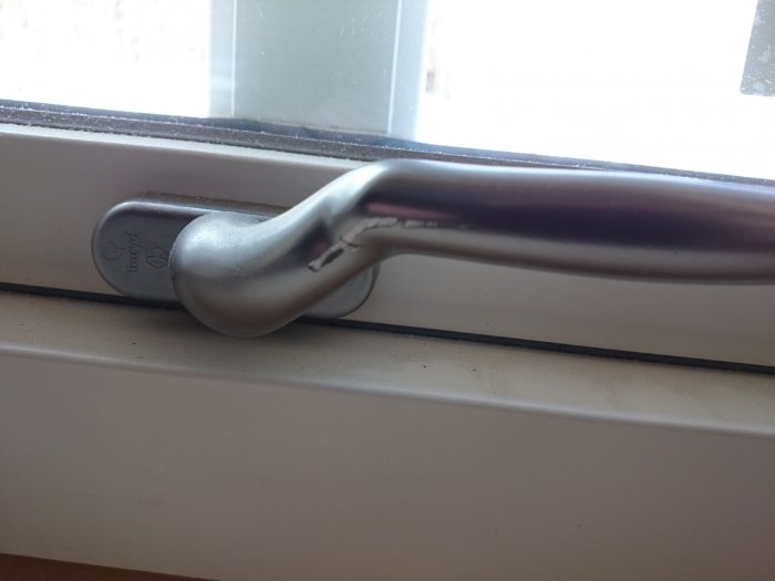 Närbild på ett fönsterhandtag med en synlig repa på metallens yta.