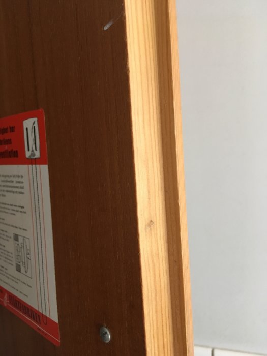 Närbild på en teakfanerad kökslucka med synliga slitage och en skruv i förgrunden.