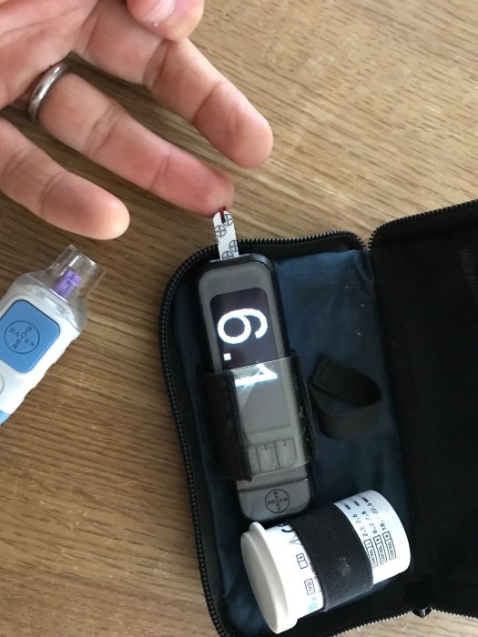 En hand som håller en blodglukosmätare med testremsor och kontrollösning.