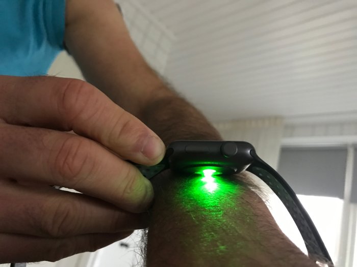 Person med Apple Watch som visar en glukossensor med grön ljusstråle på handleden.