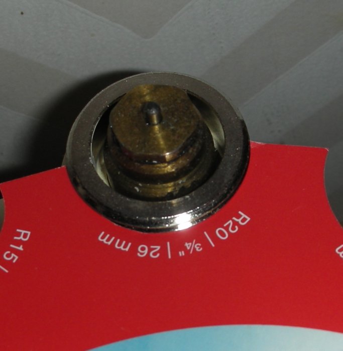 Gammal radiatorkran med misstänkt M26-gänga ovanpå en röd mätsticka för att identifiera storleken.