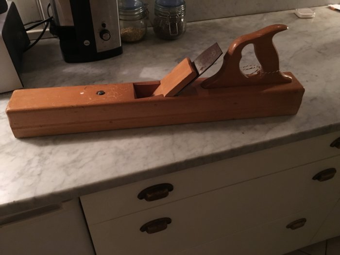 Gammal trähyvel med stål från Eskilstuna, inristat med JPBO, på ett köksbänk.