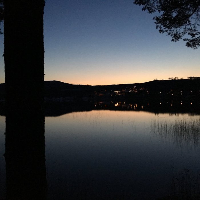 Skymningsvy över Sryrsjöbo i Leksand med stilla sjö och siluett av träd och kullar.