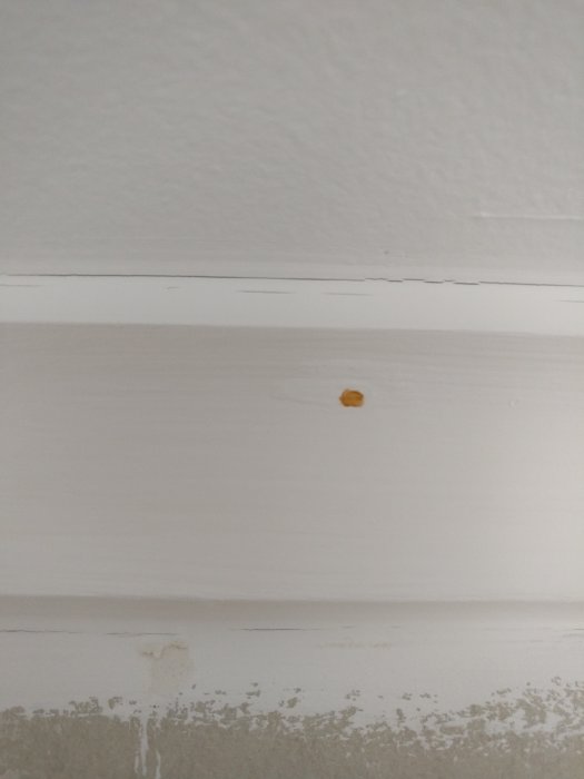Vitmålad vägg med en fläck och listverk med sprickor.