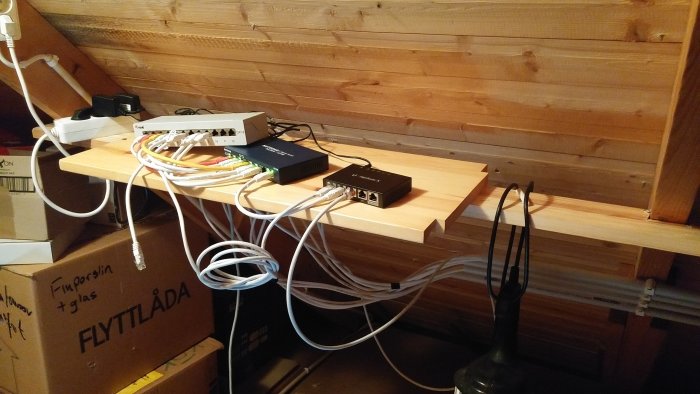 En hemmanätverkscentral med en Edgerouter X, Netgear switch, och flera ethernetkablar på en trähylla.