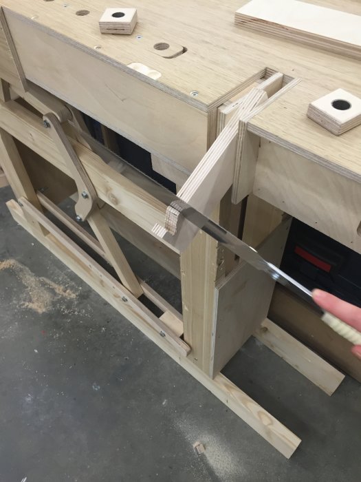 En hand som använder en japansåg för att såga i en plywoodbit på en arbetsbänk.
