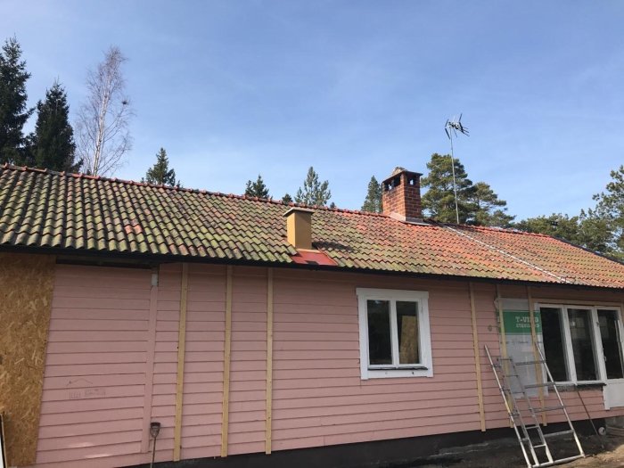 Taktegel demonteras från ett hus i ett renoveringsprojekt, med en stege lutad mot huset.