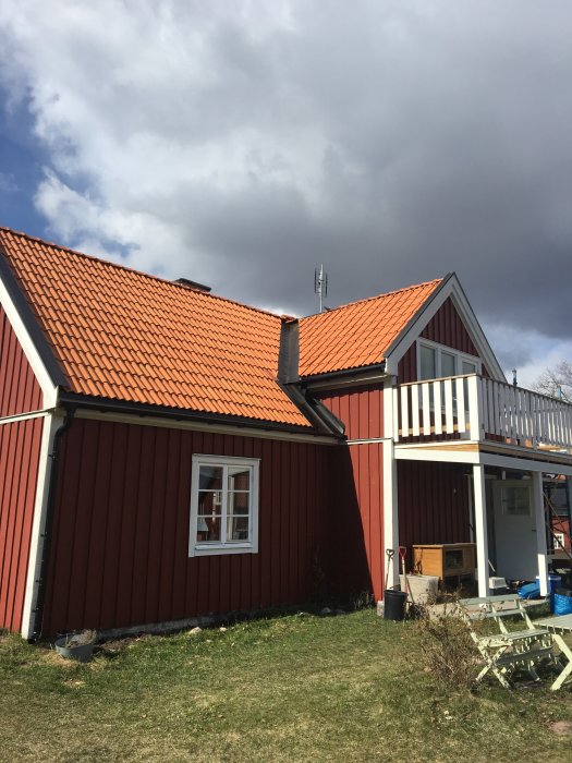 Traditionellt svenskt rött hus med vita knutar och tegeltak under en molnig himmel.