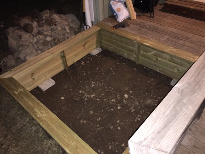 Träkonstruktion för sandlåda integrerad med trädäck, med löstagbar bräda för kattskydd.