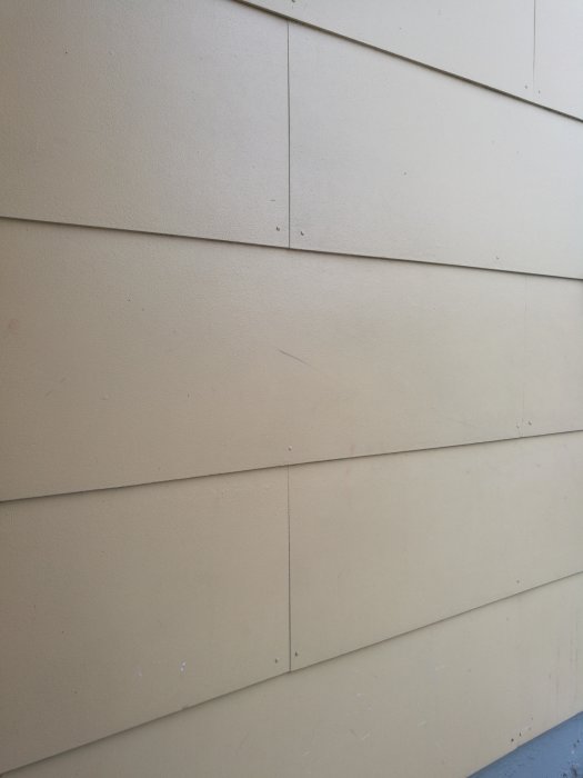 Vägg med fibersementpaneler i beige, synliga skarvar och några små fläckar, oklart målningstillstånd.