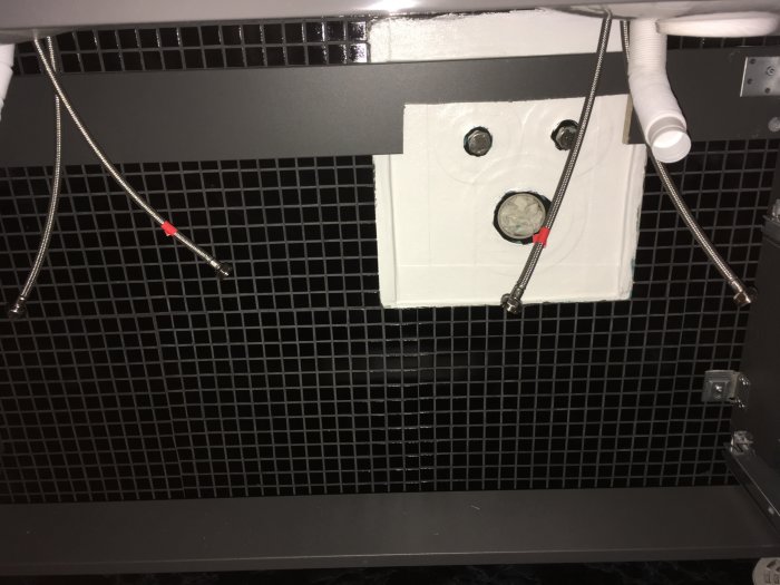 Installation under en kommod med två flexibla kopparslangar och ett avloppsrör.
