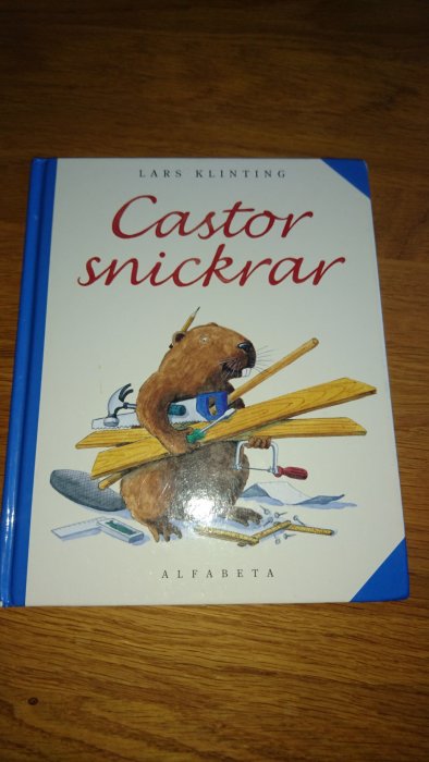 Bokomslag för "Castor snickrar" av Lars Klinting på ett träbord.