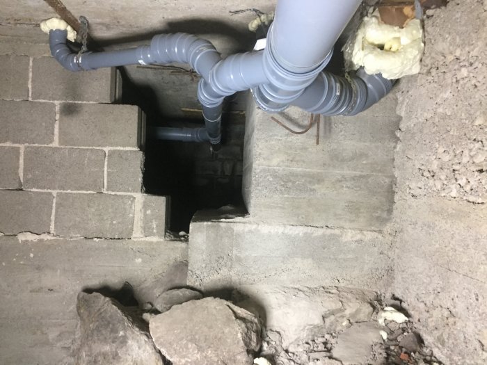 Bild på en delvis riven grundmur med synliga rörledningar och en öppning ner till en krypgrund.