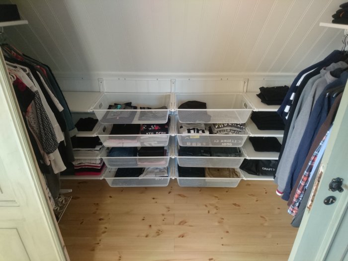 Nyrenoverad garderob med vita väggar och trägolv, inredd med IKEA hyllor och klädstänger.