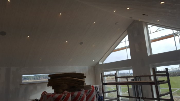 Inredning av ett rum med nyinstallerade spotlights i sluttande tak, byggmaterial och ställningar synliga.