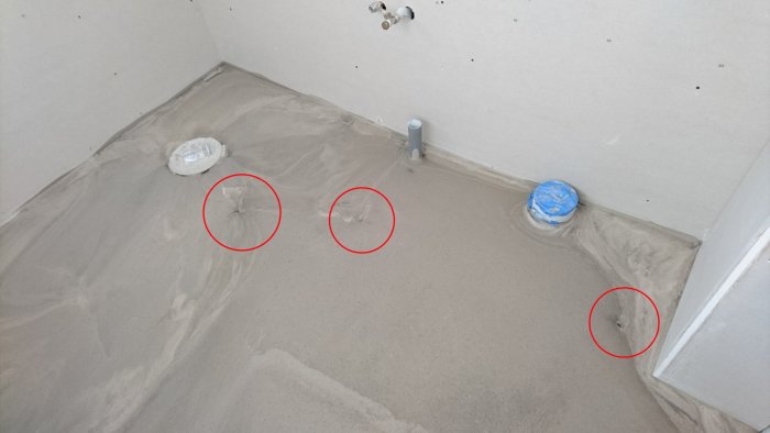 Renoverat badrumsgolv med färsk flytspackel och fyra markerade läckagepunkter.