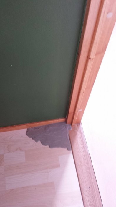 Flytspackel har läckt och stelnat på ett trägolv bredvid en vägg och dörrkarm.