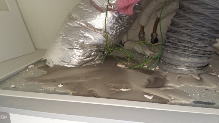Flytspackel har läckt och stelnat på vitvarans topp, kablar och ventilationsslang syns.