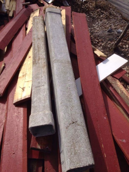 Eternitrör och byggmaterial som råspont och brädor, avlägsnade från ett renoveringsprojekt, ligger på marken.