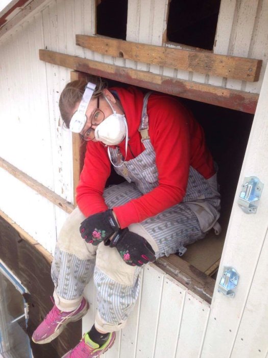 Person i skyddsutrustning tar en paus i en fönsteröppning under en husrenovering.