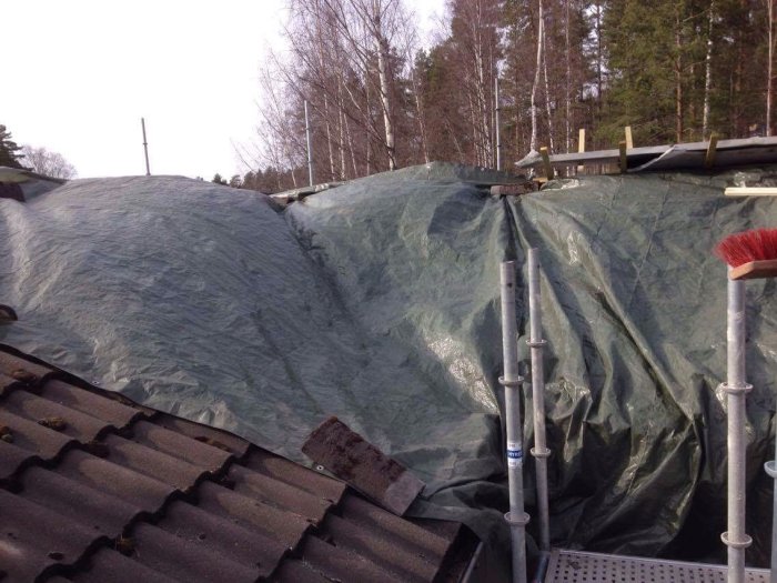 Presenning över tak där skorstenshuvar tagits bort, rör och kost syns.