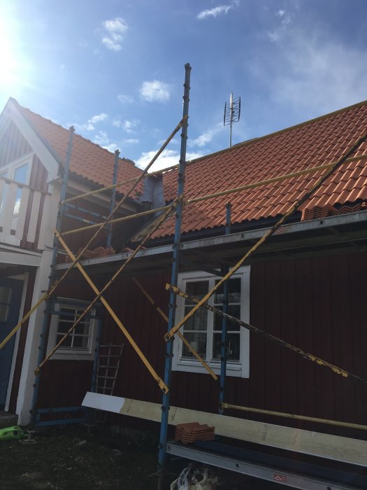 Ställning framför röd trähusfasad under solig himmel, möjlig renovering pågår.