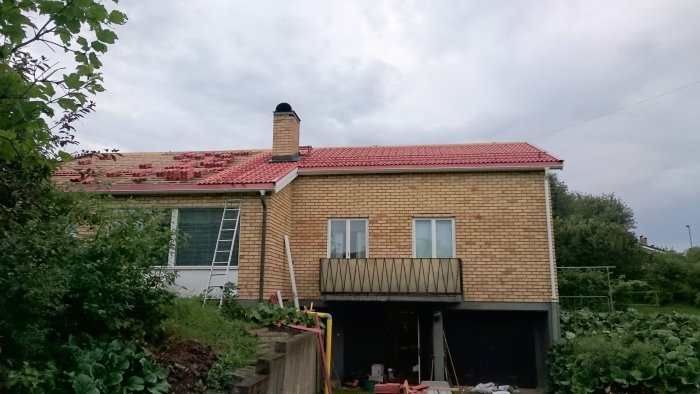 Hus med tegeltak under renovering, förberett för installation av solceller, stegar mot fasad.